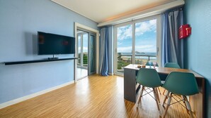 A modern room with a TV, a dining table with chairs, a balcony with a view of the sea, and a red emergency box on the wall. - Goseong Bokee House (Goseong)