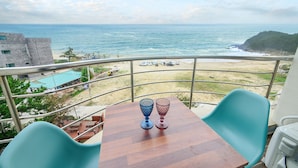 A balcony with a wooden table and two chairs, overlooking a beach with parked vehicles and a view of the ocean. - Goseong Bokee House (Goseong)