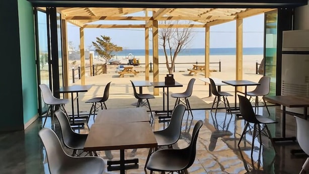 A beachside cafe with outdoor seating, a wooden pergola, and a view of the beach and ocean. - Goseong Bokee House (Goseong)