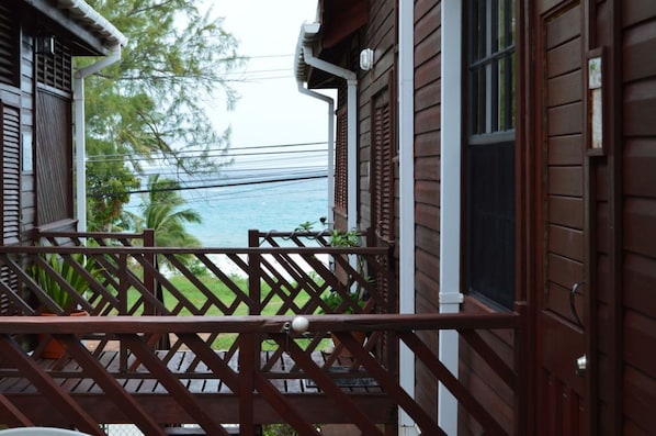 A wooden house with a balcony overlooking a body of water and greenery. - Yellow Bird Apartment in Blue Ocean Cottage in Silver Sands (Silver Sands)
