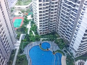 A high-rise building with multiple balconies and a central swimming pool surrounded by greenery.