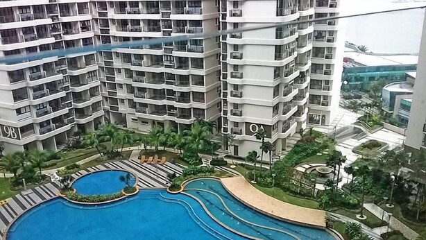 A high-rise building with multiple balconies and a central swimming pool area with palm trees and lounge chairs. - Pool View Suites (Johor Bahru)