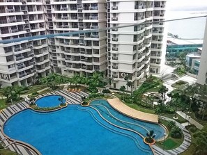 A high-rise building with multiple balconies and a central swimming pool area with palm trees and lounge chairs. - Pool View Suites (Johor Bahru)