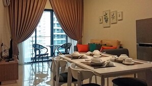 A modern living room with a dining area, large windows with curtains, a sofa with cushions, and a refrigerator. - Pool View Suites (Johor Bahru)
