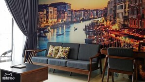 A living room with a sofa, two armchairs, a coffee table, and a large wall mural of a cityscape. - Pool View Suites (Johor Bahru)