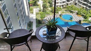 A balcony with wicker chairs and a glass table, overlooking a swimming pool and lush greenery. - Pool View Suites (Johor Bahru)
