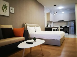 Un espacio habitable moderno y compacto con sofá, cama, una mesita y una kitchenette al fondo.