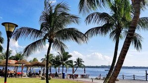 Eine Strandlage mit Palmen, Sitzgelegenheiten im Freien und Blick auf das Meer.