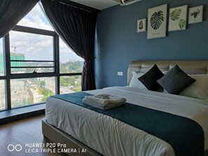 A modern hotel room with a large bed, a view of the city through a window, and framed botanical prints on the wall. - City View Suites (Johor Bahru)