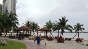 Ein Küstenabschnitt mit Reetdachschirmen, Liegestühlen und einem Weg zum Strand.