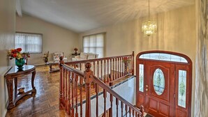 Een ruime woonkamer met een houten trap, een groot raam en een kroonluchter.