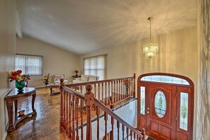 A spacious living room with a wooden staircase, a large window, and a chandelier.