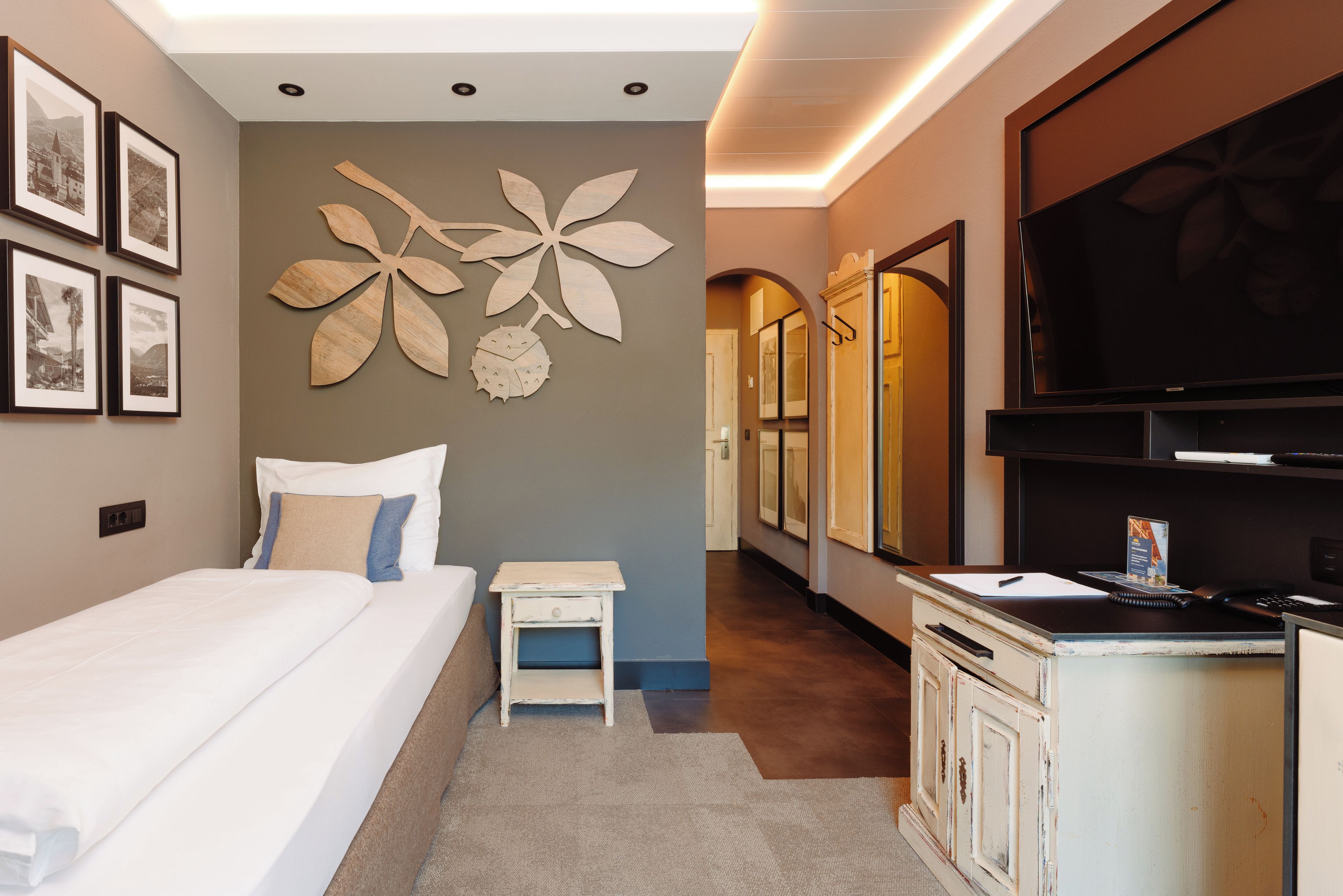 A hotel room with a bed, a small bedside table, a wall-mounted TV, and framed pictures on the wall.