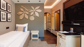 A hotel room with a bed, a small bedside table, a wall-mounted TV, and framed pictures on the wall.