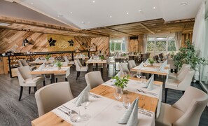 A restaurant with wooden walls, white tables, and chairs. - MONDI Hotel Tscherms (Cermes)