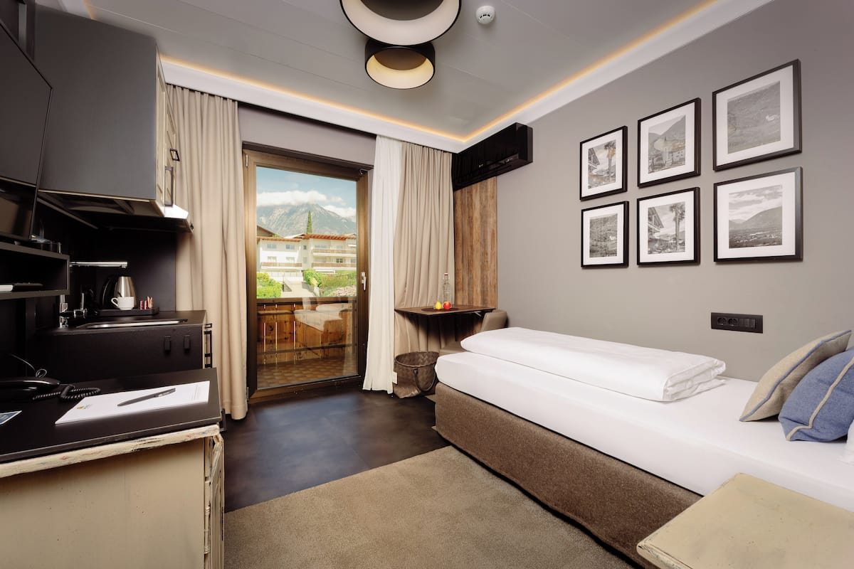 A modern hotel room with a bed, desk, and a view of a mountain and building through a glass door.