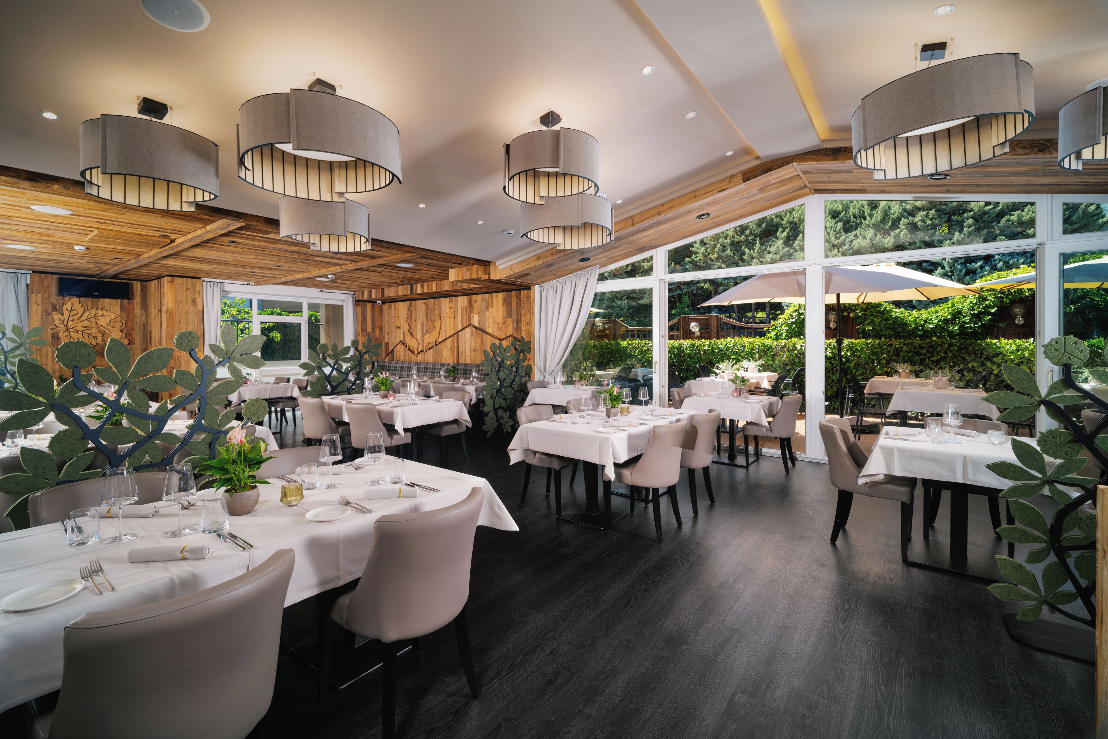 A restaurant with round tables, pendant lighting, and a view of greenery outside.