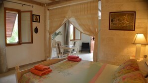 Une chambre avec un lit, un bureau et une chaise. Il y a une fenêtre avec des stores, une lampe et un tableau au mur.