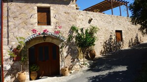 A stone building with a wooden door and windows, a tiled roof, and potted plants.