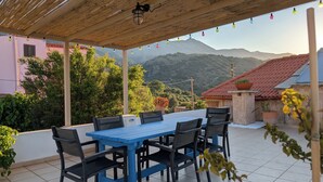 A covered patio with a blue table and chairs, surrounded by greenery and buildings with red roofs.