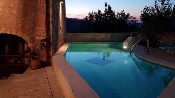 A swimming pool with a tiled deck, a small slide, and a stone wall.