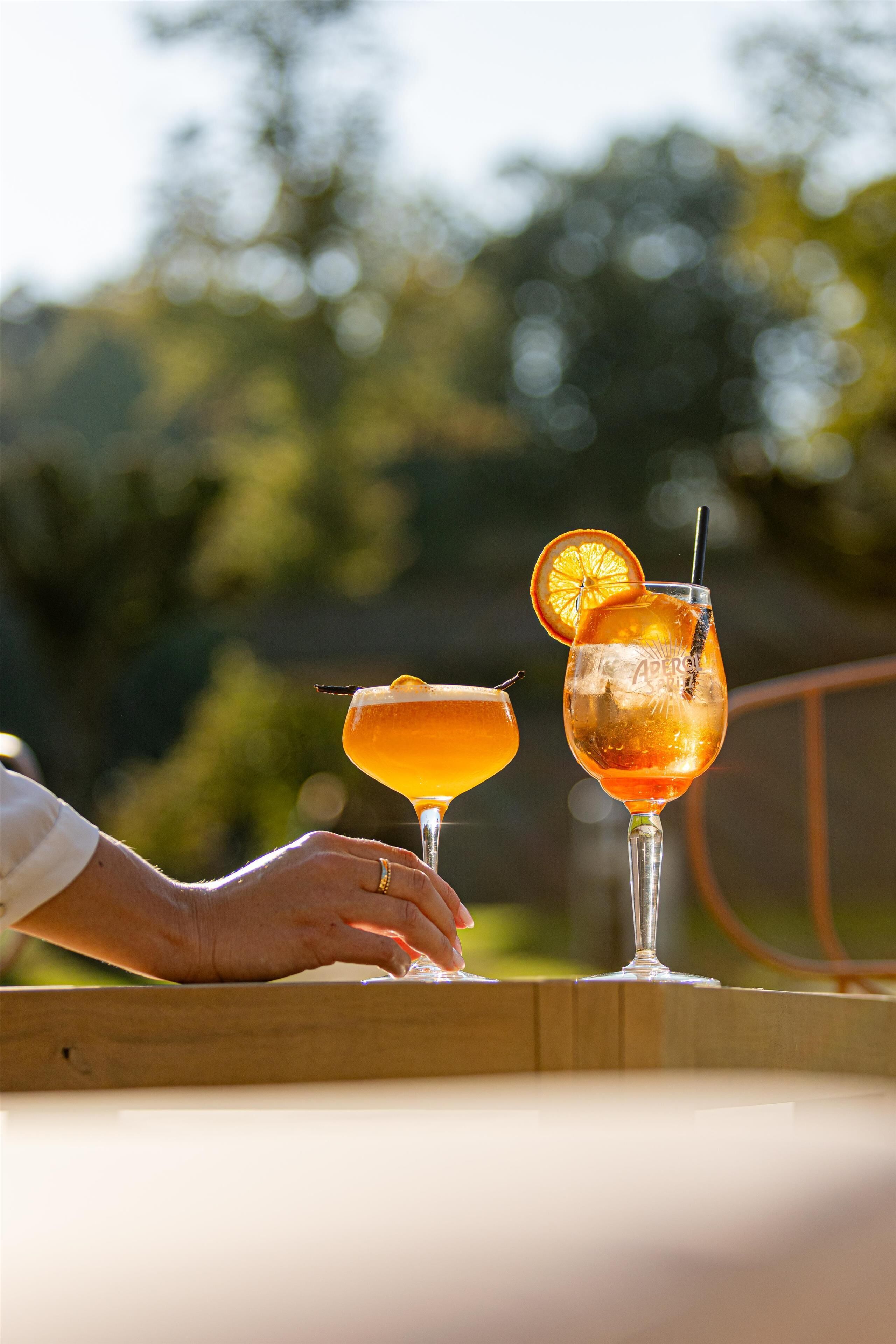 Two cocktails on a table with a blurred outdoor background.