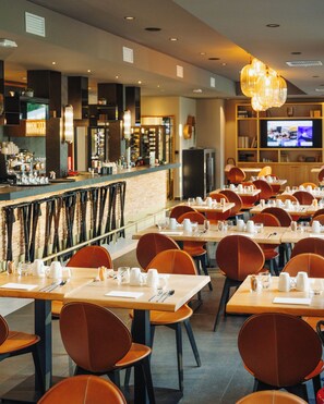A restaurant with multiple tables and chairs, a bar area, and a television screen. - Domaine de Dolomieu, BW Premier Collection (Dolomieu)