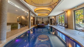 Un espace piscine intérieur moderne, doté d’un élément aquatique central, de coins salon et d’un comptoir d’accueil.
