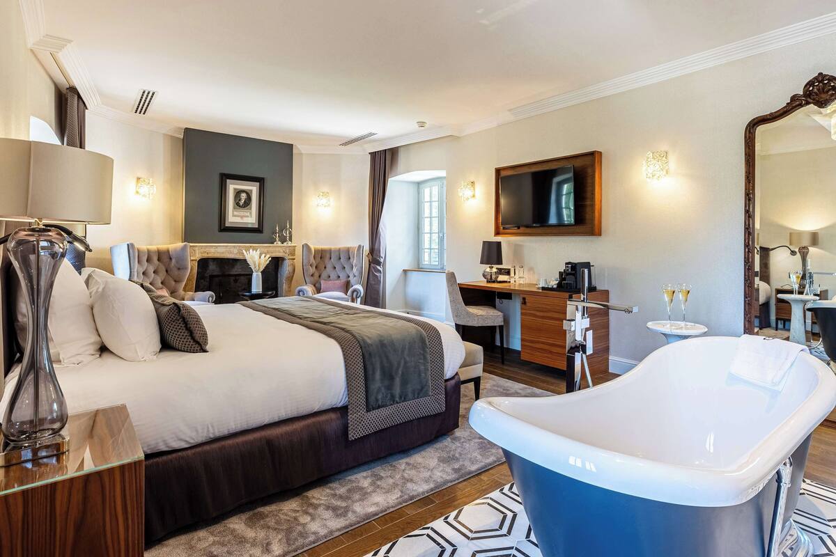 Una habitación de hotel con una cama grande, un escritorio, una silla, una bañera y un televisor.