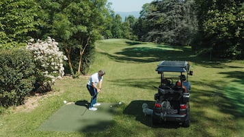 A golf course with a putting green, a golf cart, and a dog.