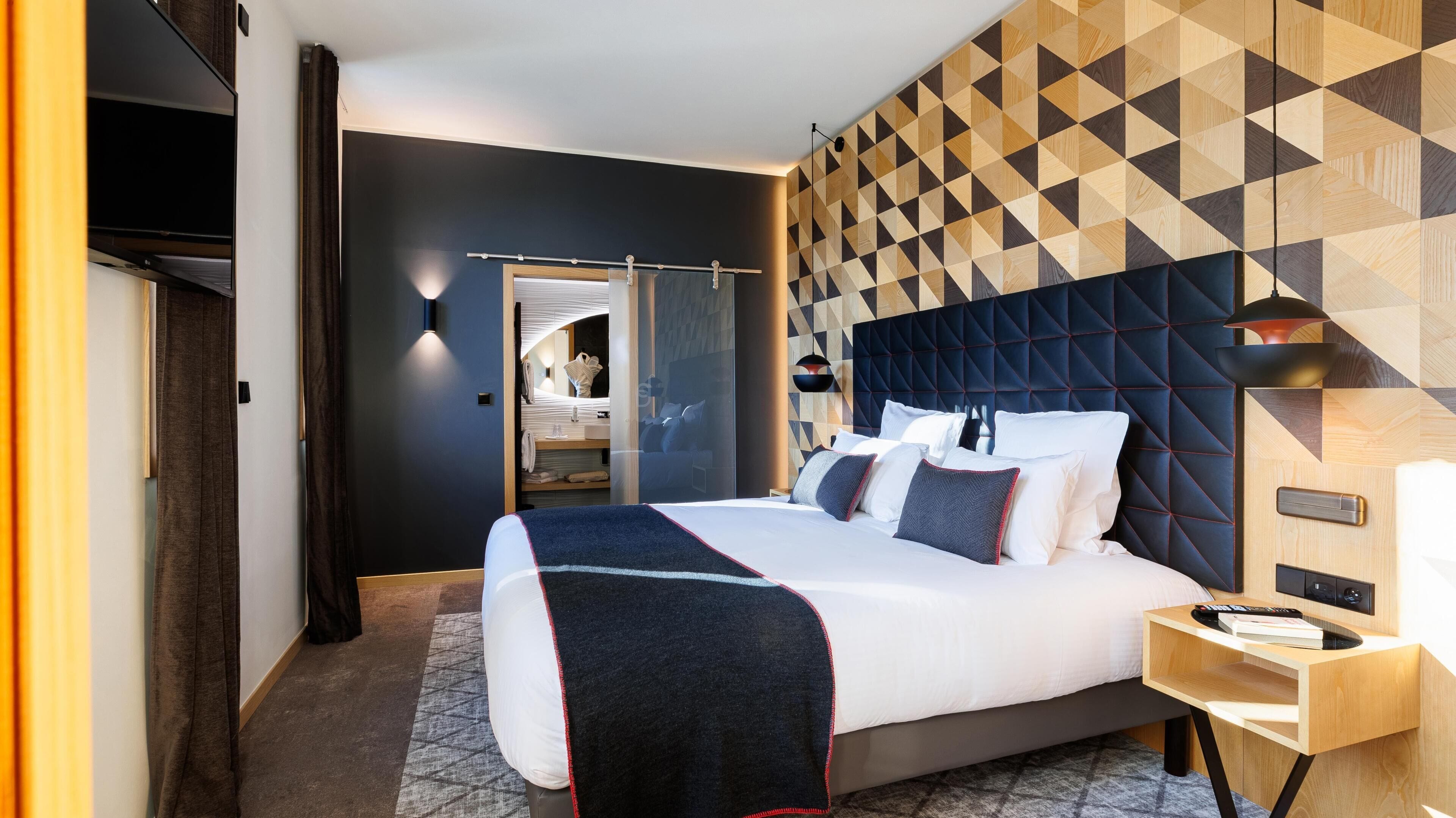 Una habitación de hotel moderna con una cama grande, una mesita de noche, un armario y una pared con estampado geométrico.