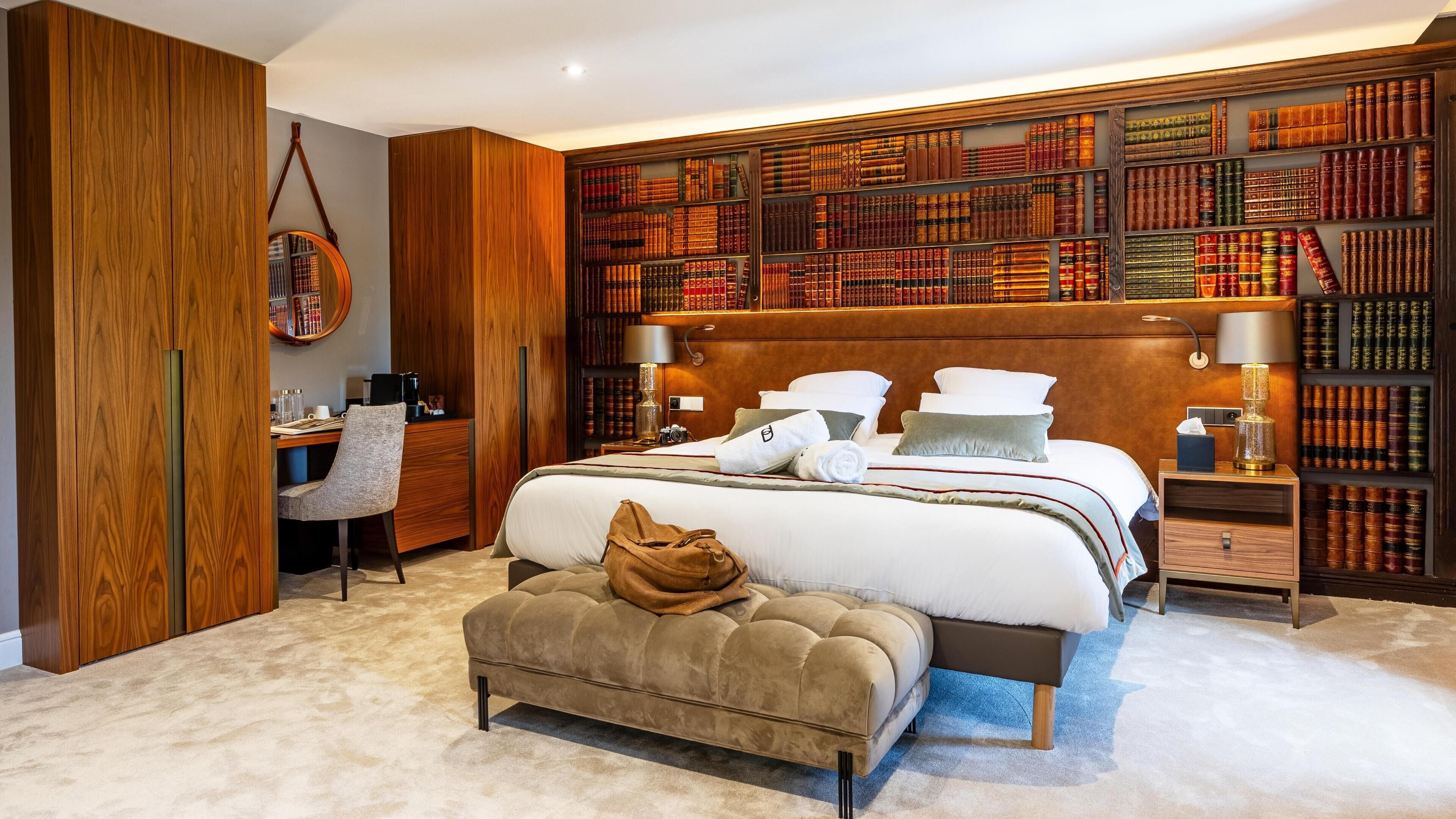 Un dormitorio con una cama grande, un escritorio, una silla, una estantería y un espejo redondo.