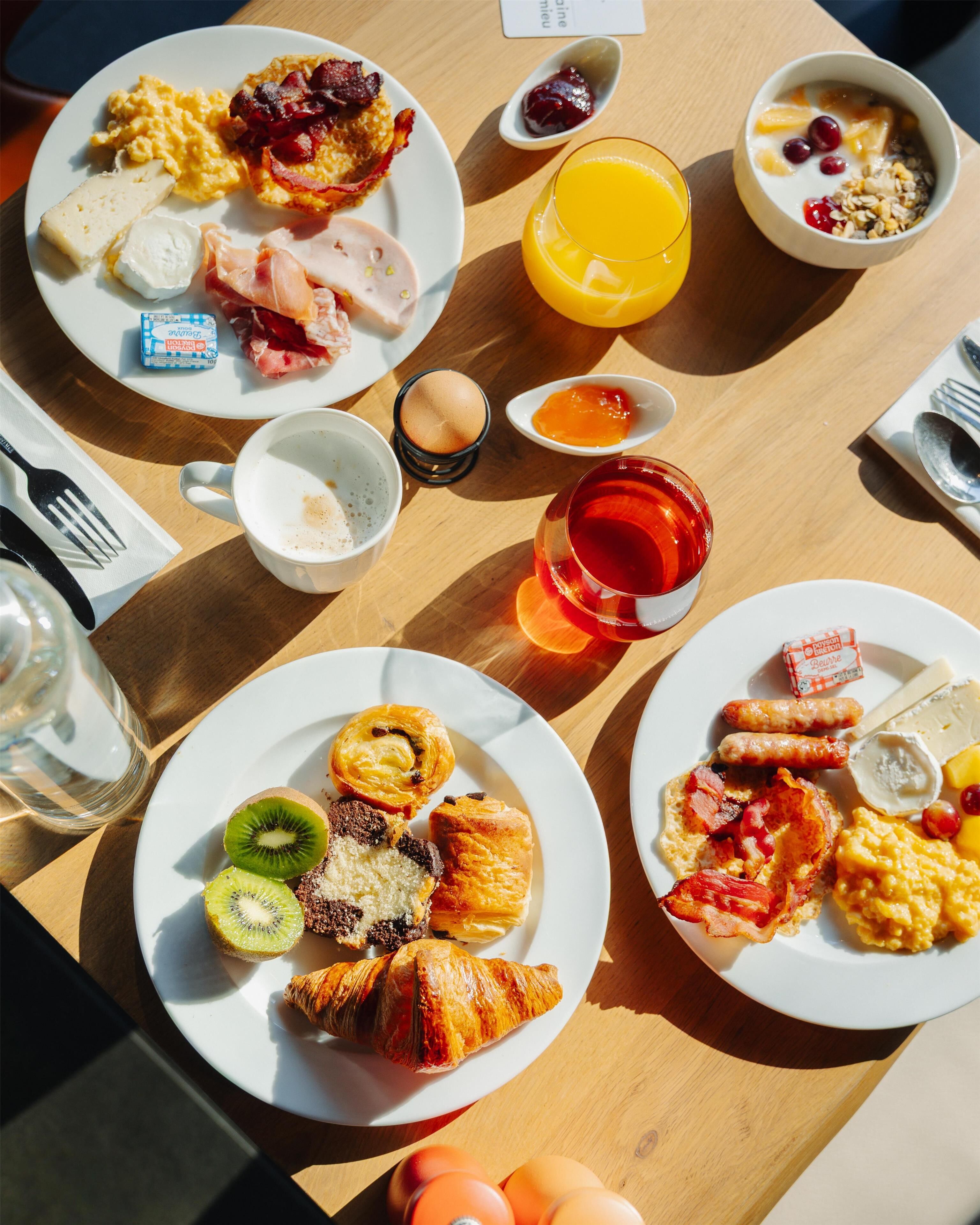A breakfast setting with various dishes, including eggs, bacon, pastries, and fruit.