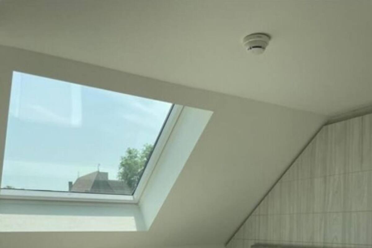 Un dormitorio con tragaluz, cama con ropa de cama blanca, cabecera y mesita de noche.