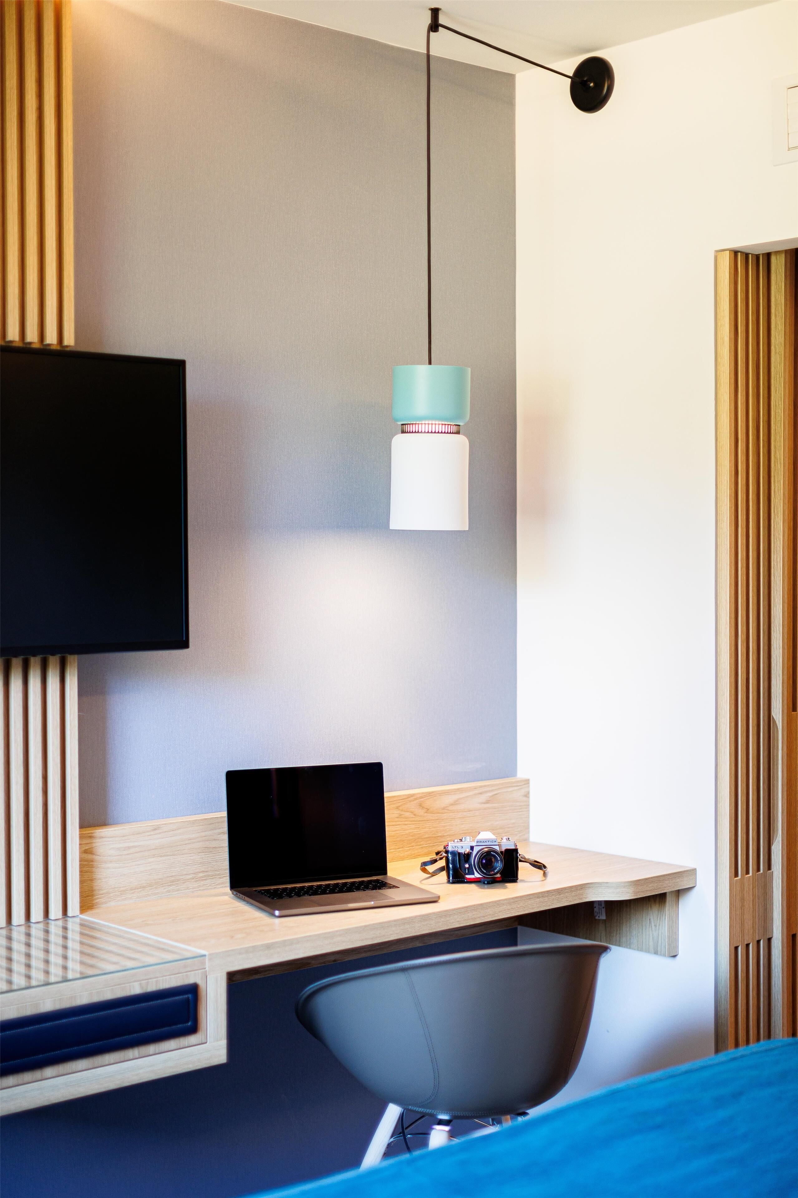 A modern room with a flat-screen TV mounted on the wall, a desk with a laptop, a camera, and a chair.