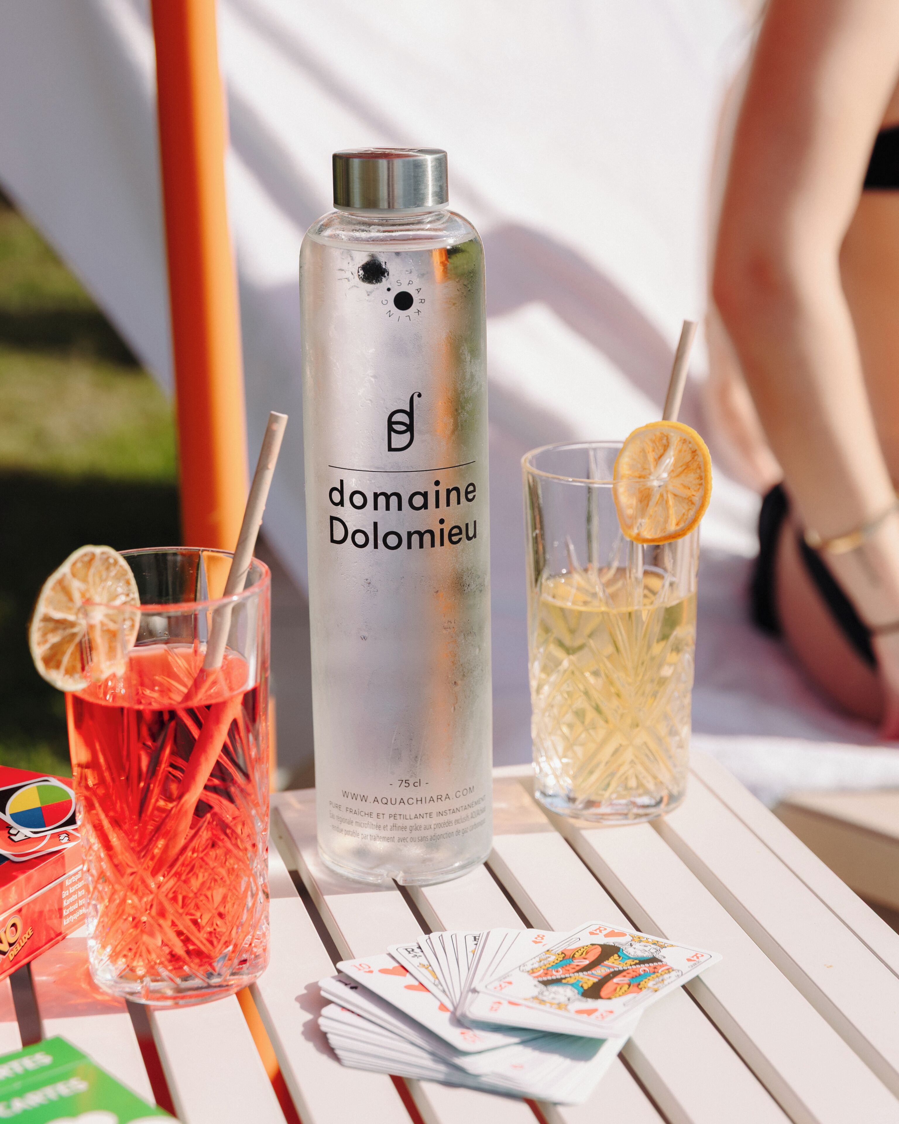 A bottle of domaine Dolomieu, two glasses with straws, and playing cards on a white table.