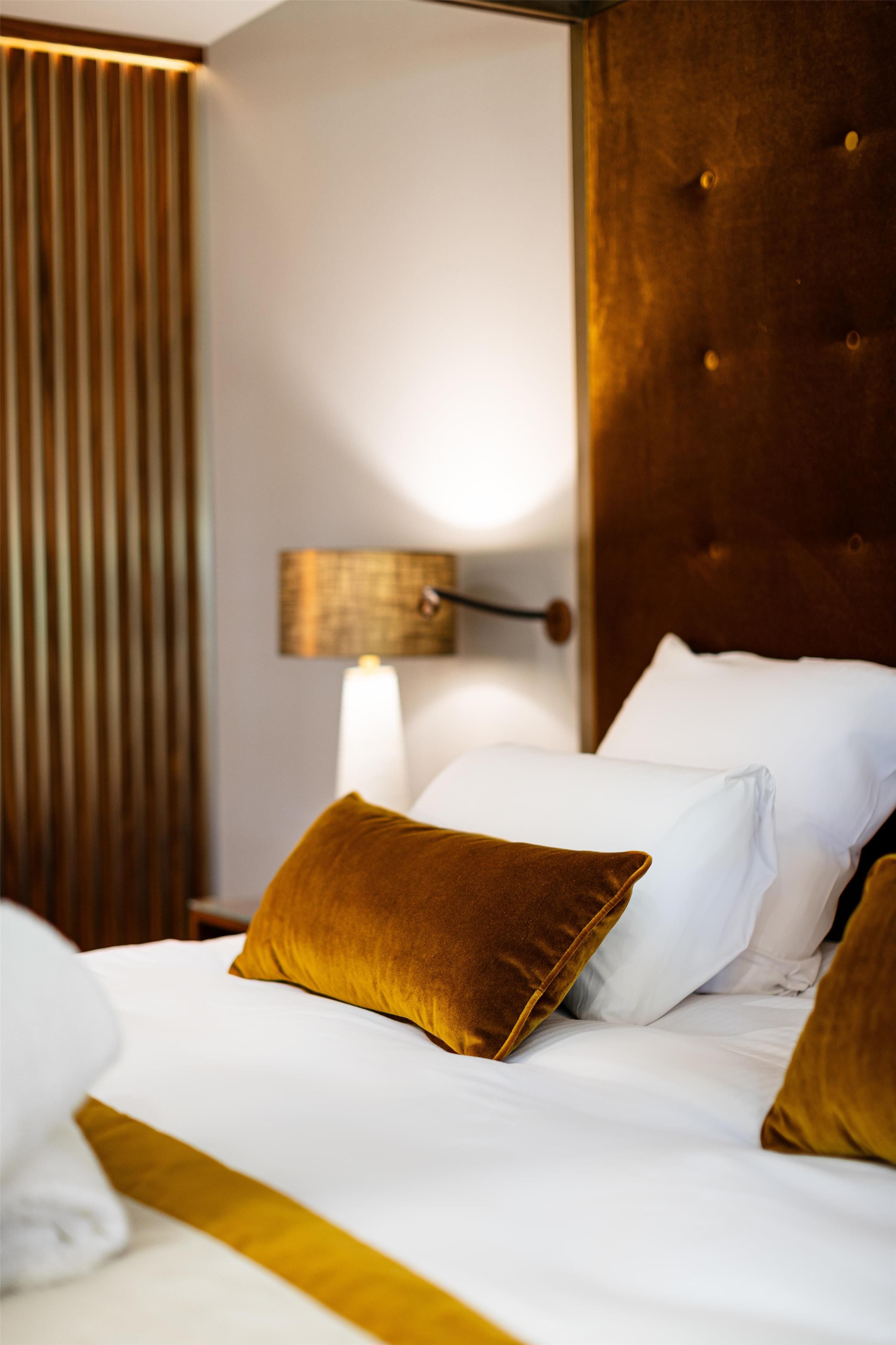 A neatly made bed with white linens and two pillows, one of which is a mustard-colored throw.