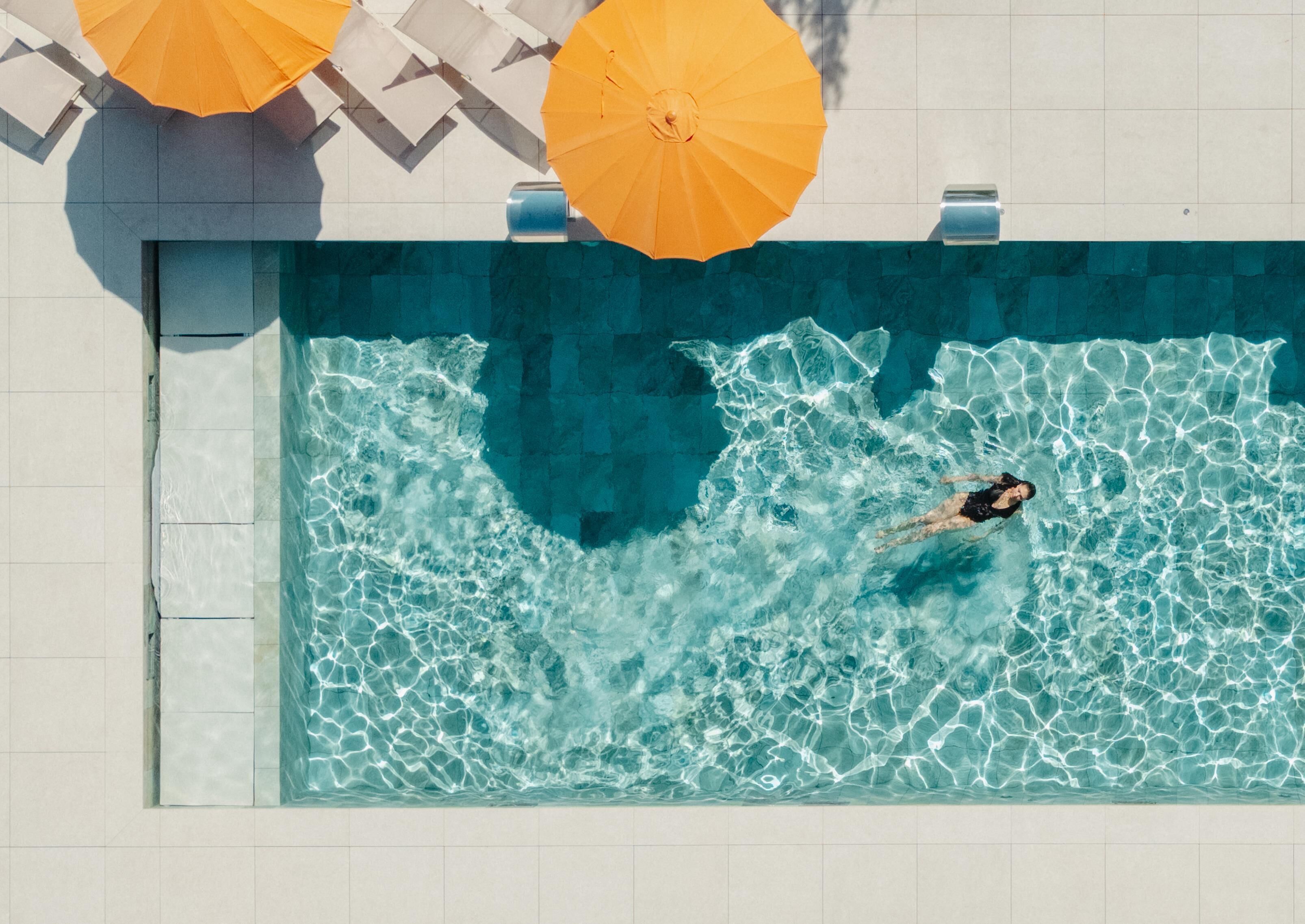 A swimming pool with clear water, a person swimming, and two yellow umbrellas.