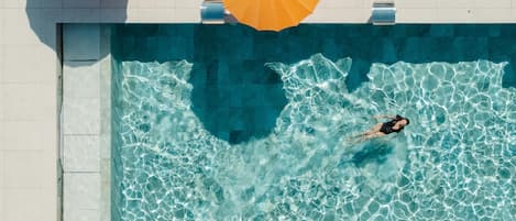 A swimming pool with clear water, a person swimming, and two yellow umbrellas.