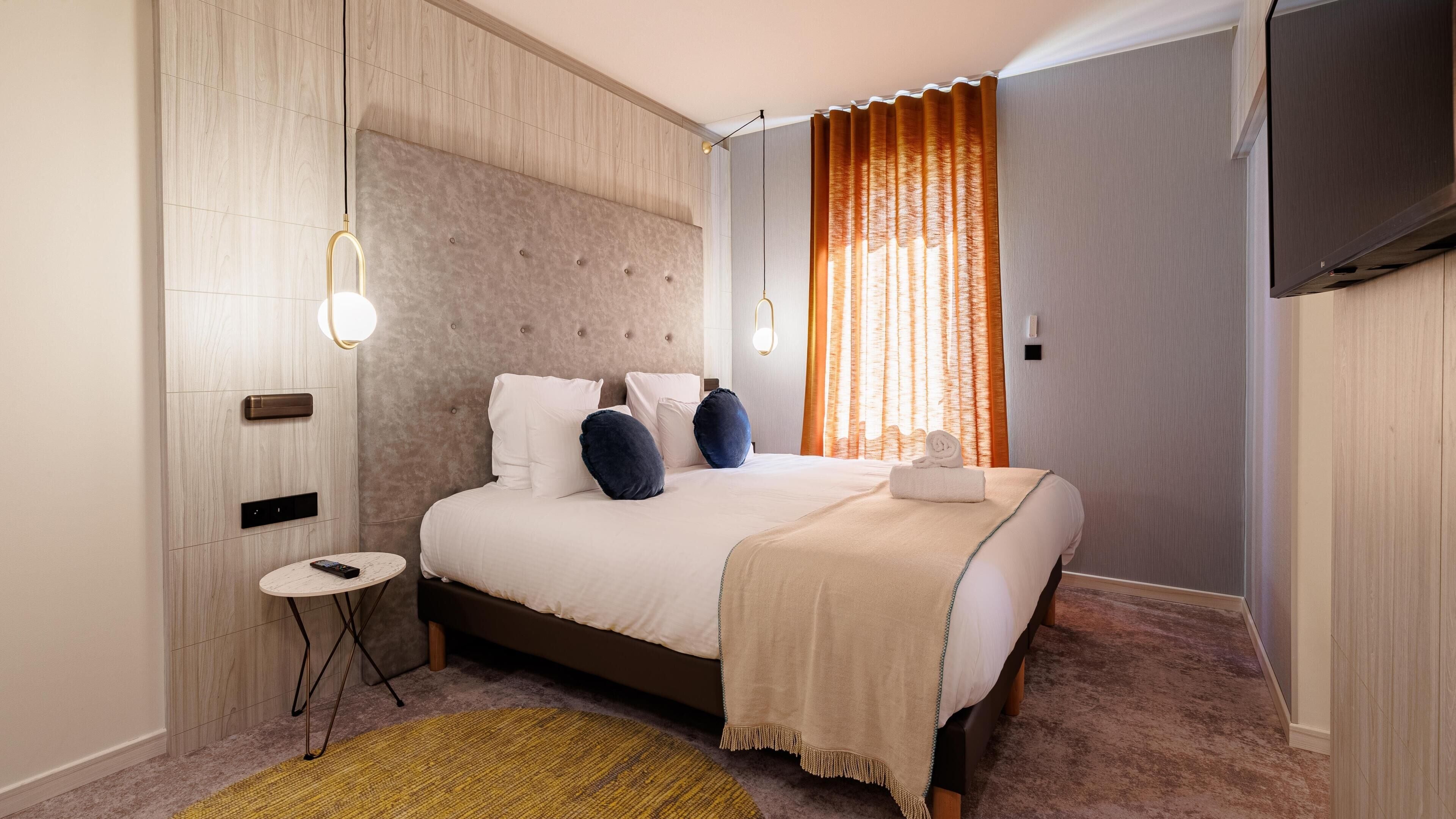A hotel room with a bed, bedside table, and a TV mounted on the wall.