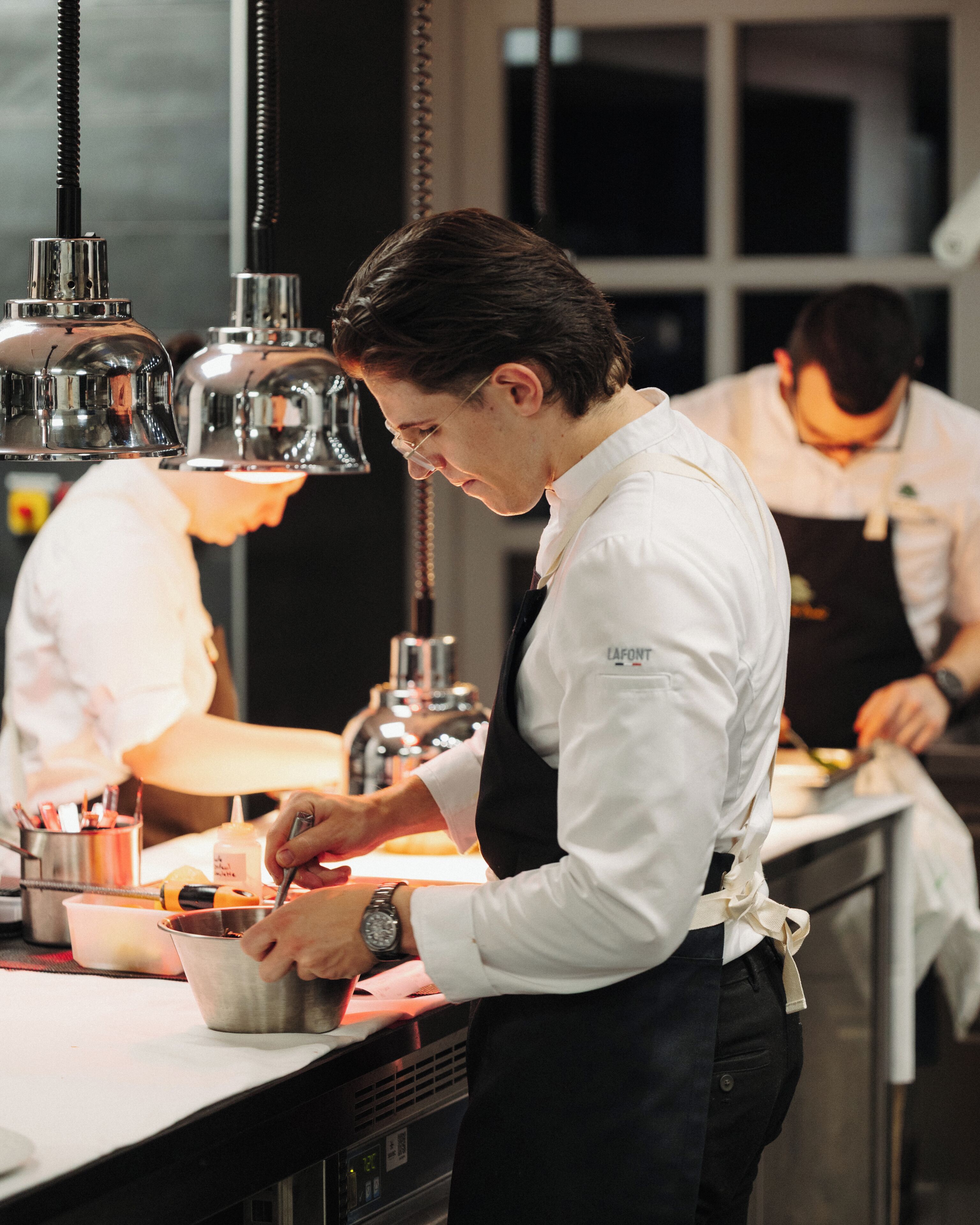Un chef preparando comida en una cocina profesional, con electrodomésticos de acero inoxidable y atención centrada en tareas culinarias.