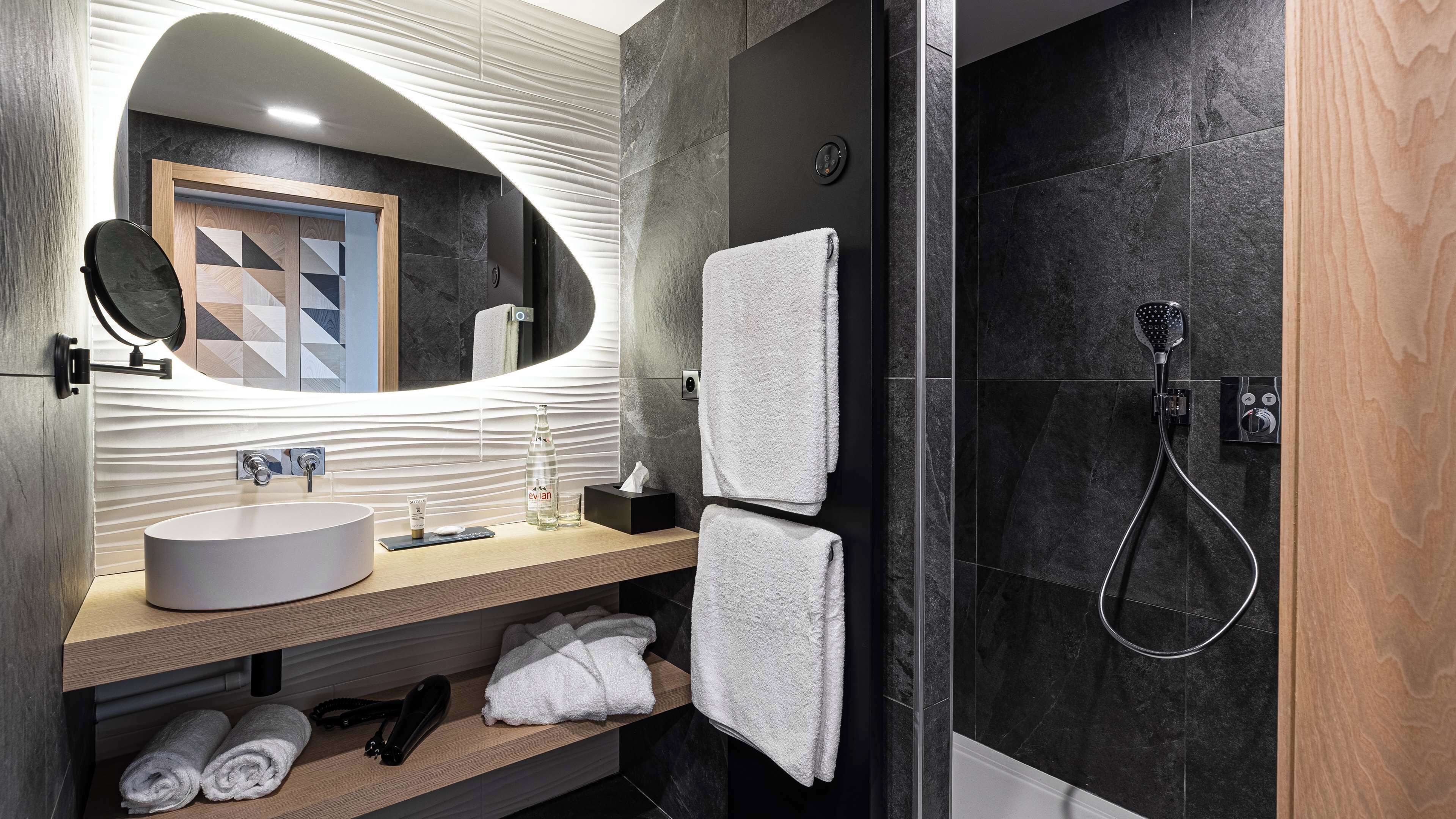 Un baño moderno con un espejo ovalado grande, un lavamanos redondo y una ducha con cabezal de ducha manual.