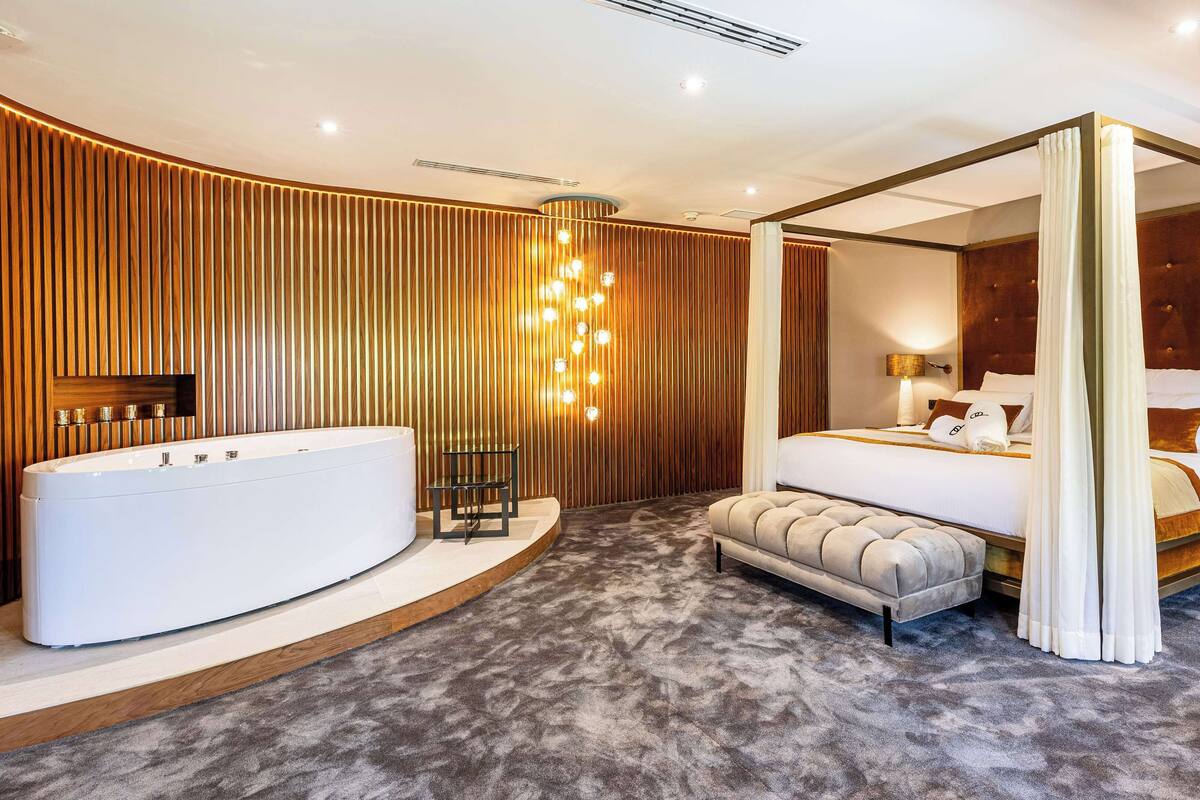Un dormitorio moderno con una cama grande, una bañera independiente y una cama con dosel original.
