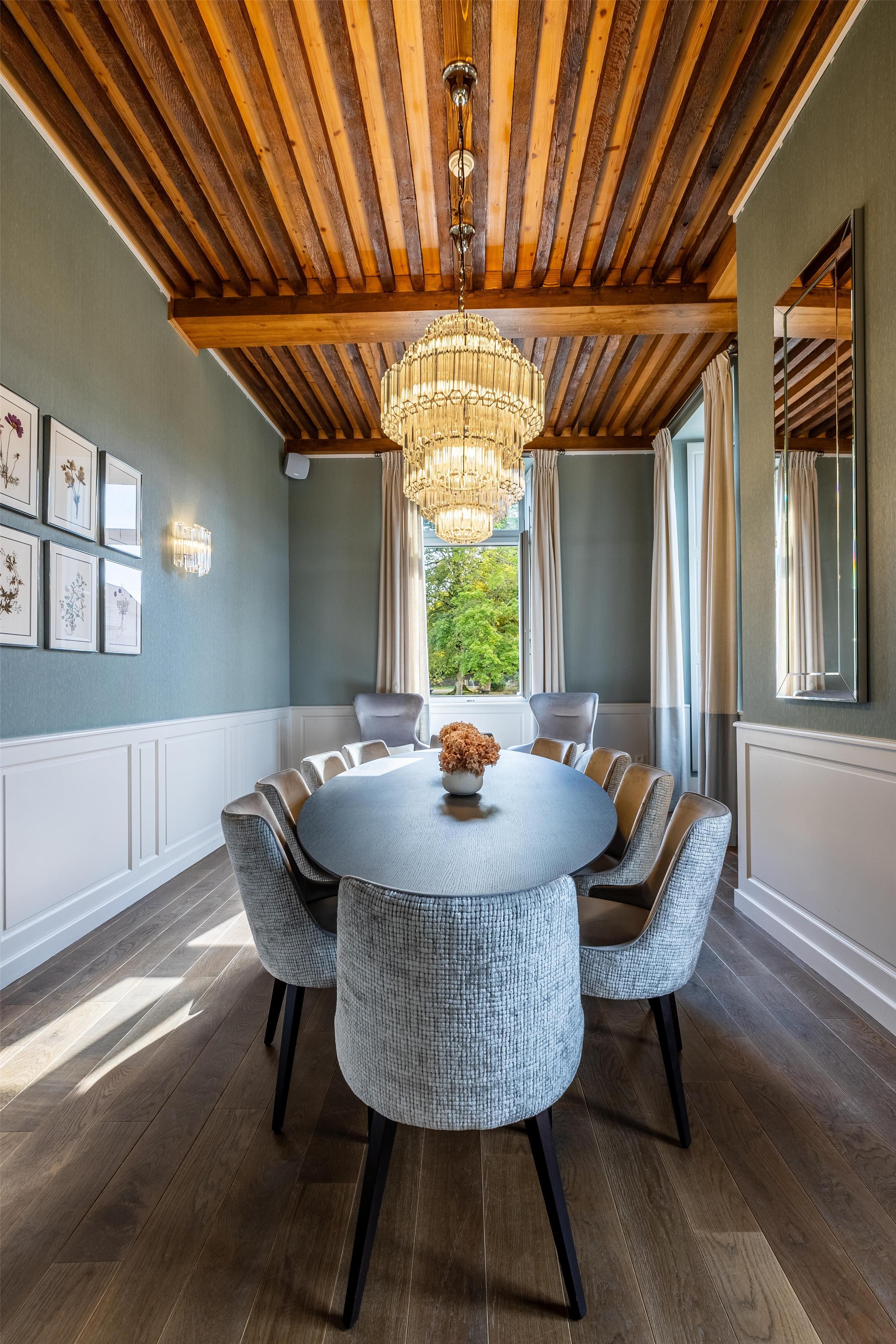 Ein Essbereich mit einem runden Tisch, gepolsterten Stühlen, einer Chandelierleuchtre und gerahmten Kunstwerken an der Wand.
