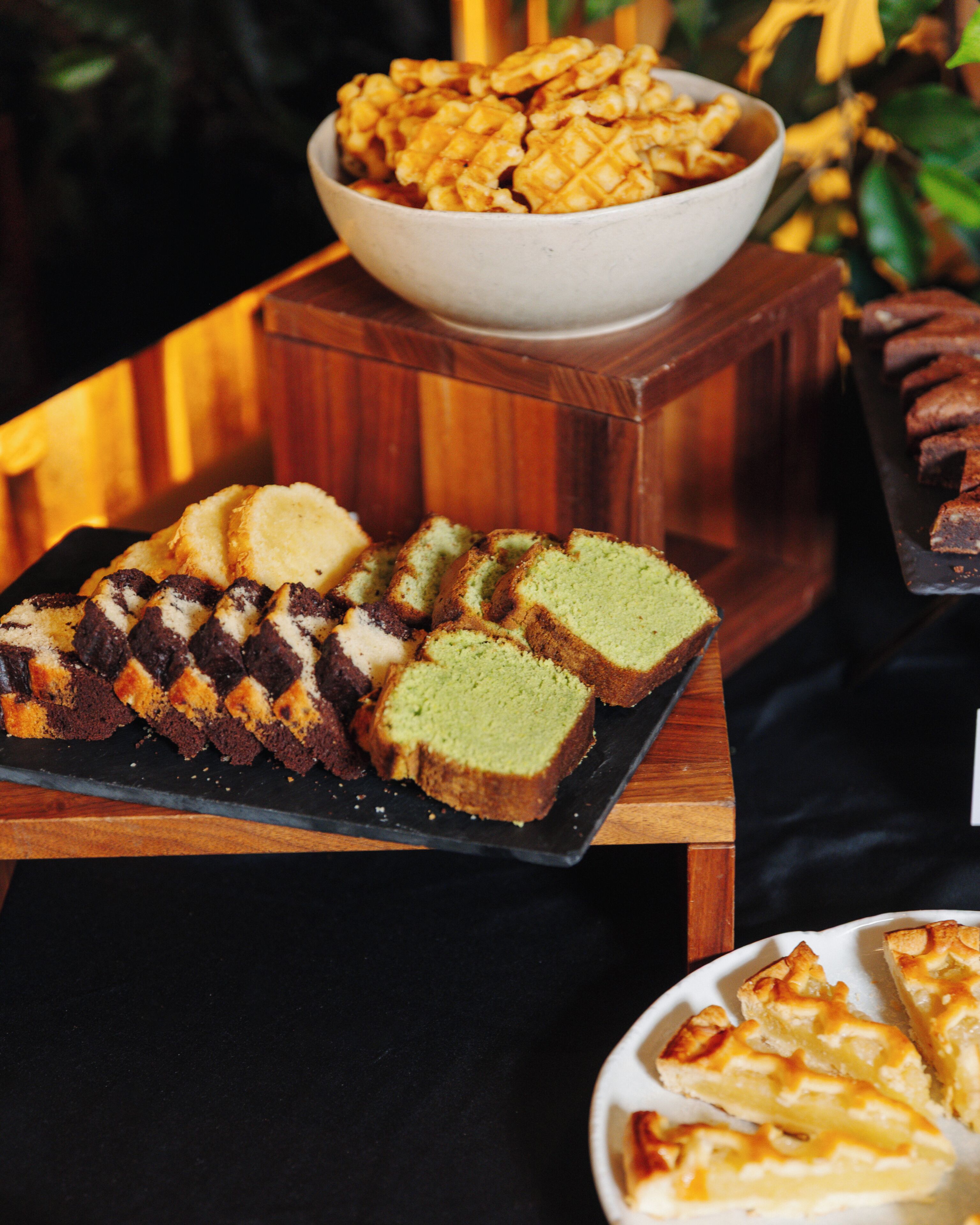 A variety of desserts on a wooden table, including slices of cake and a bowl of waffles.