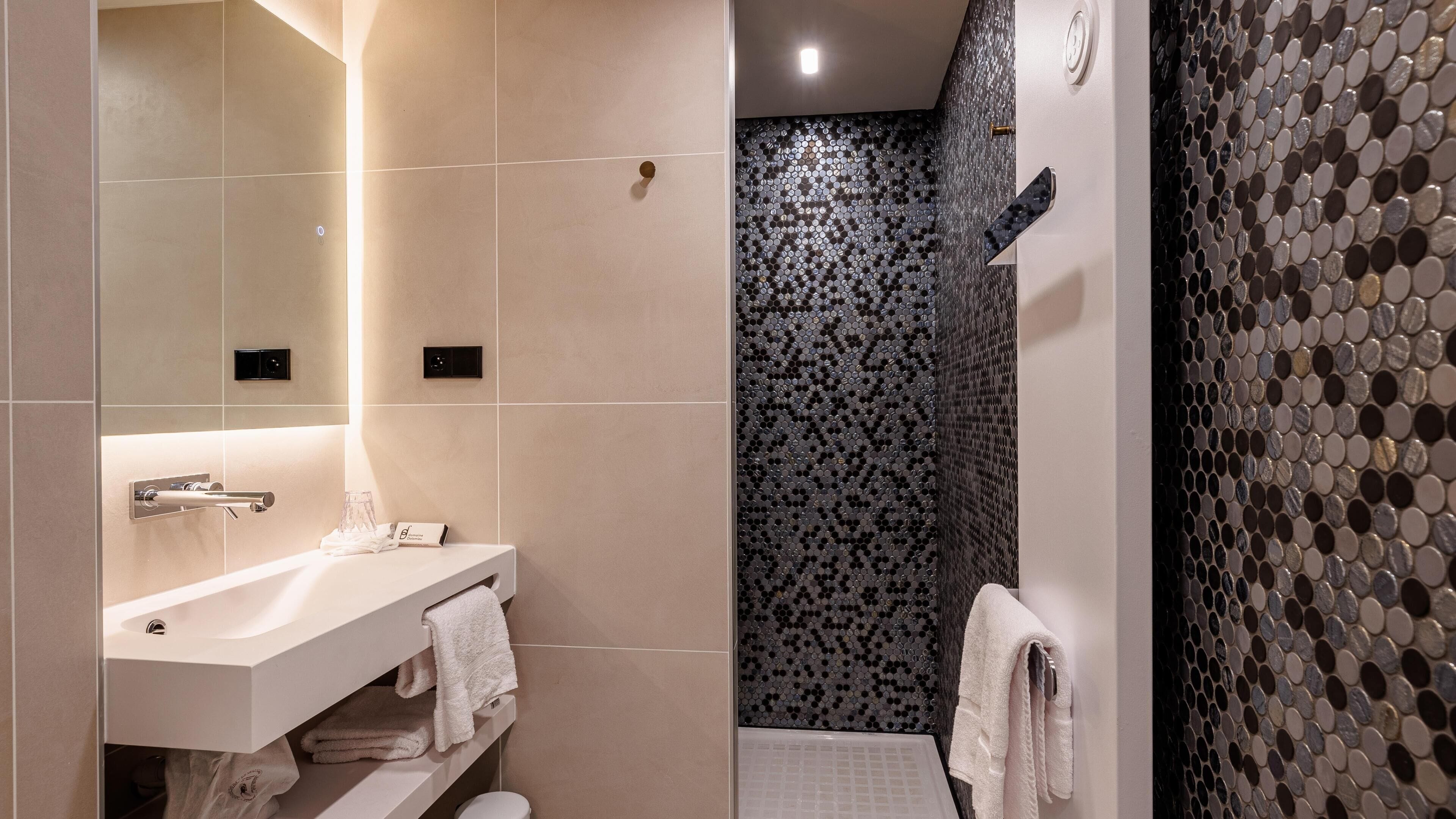 A bathroom with a white sink, towel rack, and a shower area with a patterned wall.