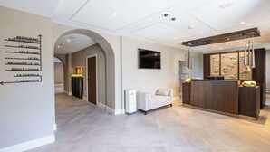 A hotel lobby with a reception desk, a sofa, a TV, and a wall sign indicating amenities like a restaurant and spa. - Domaine de Dolomieu, BW Premier Collection (Dolomieu)