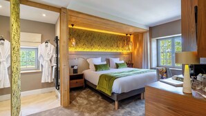 A modern bedroom with a large bed, wooden headboard, and a view of greenery through the window.
