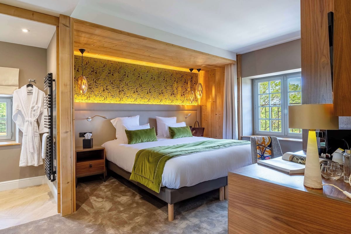 Un dormitorio moderno con una cama grande, cabecera de madera y vistas a la vegetación por la ventana.