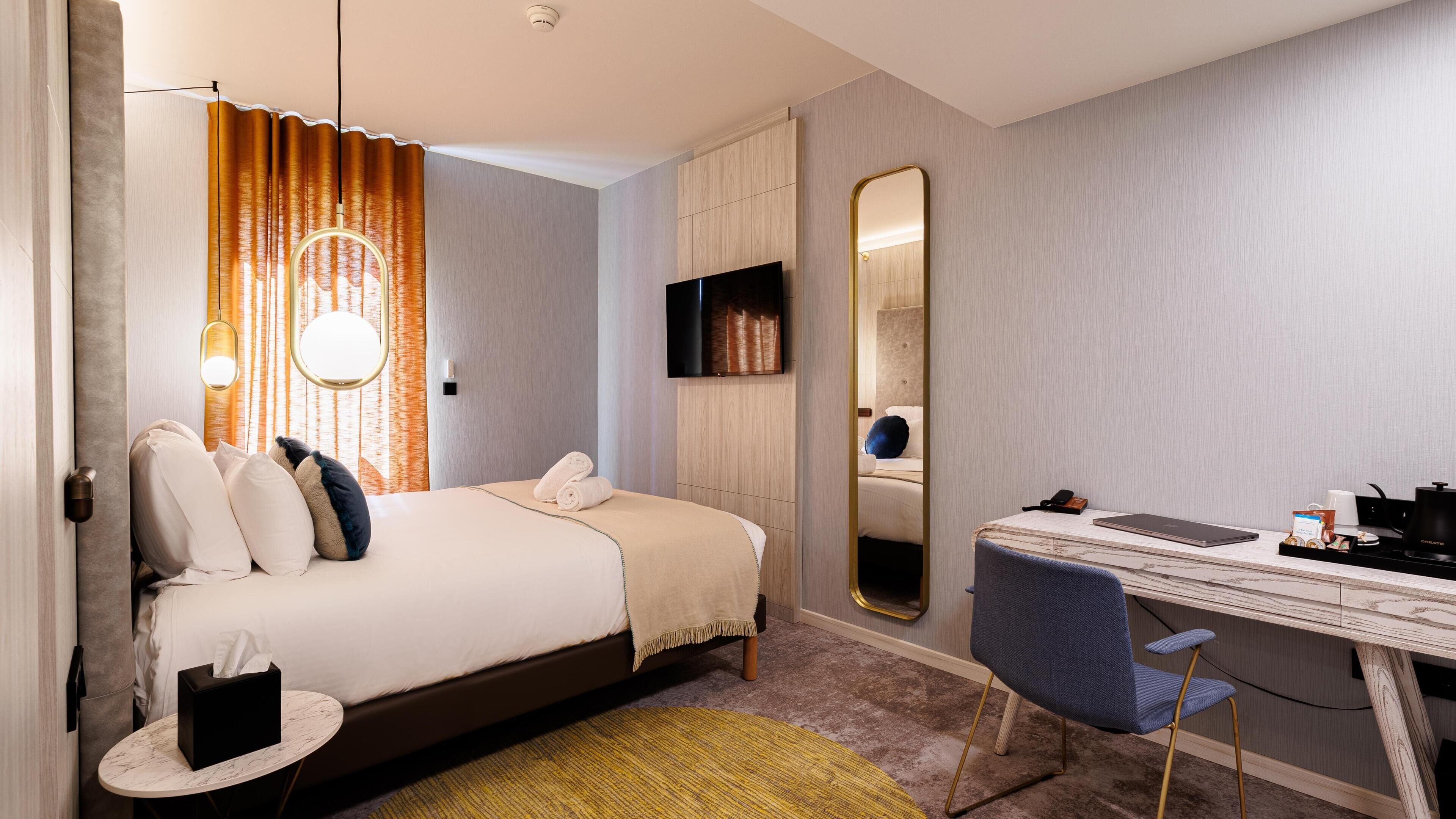 Une chambre d’hôtel comprenant un lit, une table de chevet, une chaise, un bureau et un grand miroir.